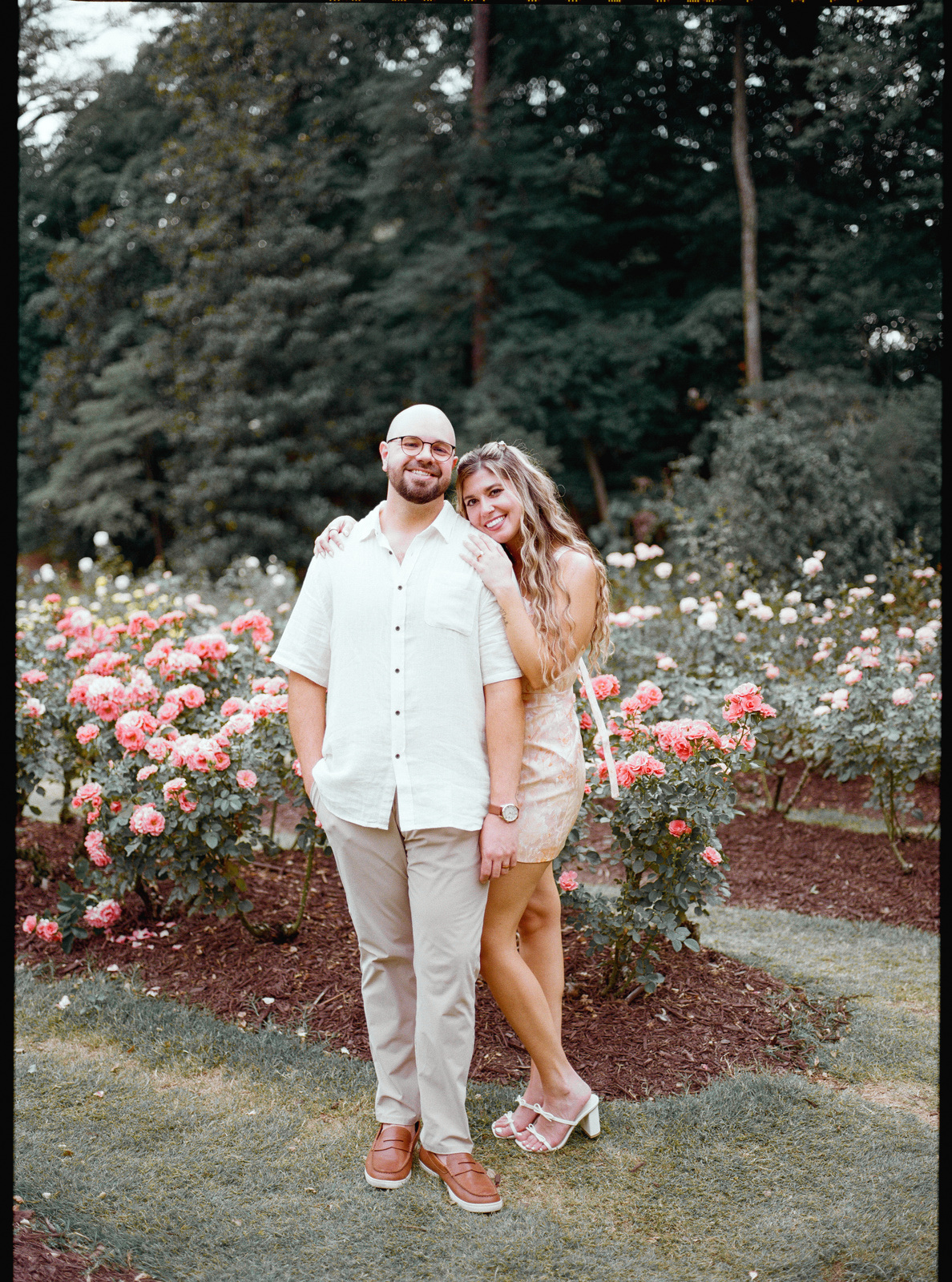 Arm in arm on the grass, with banks of coral and pink roses either side of them.