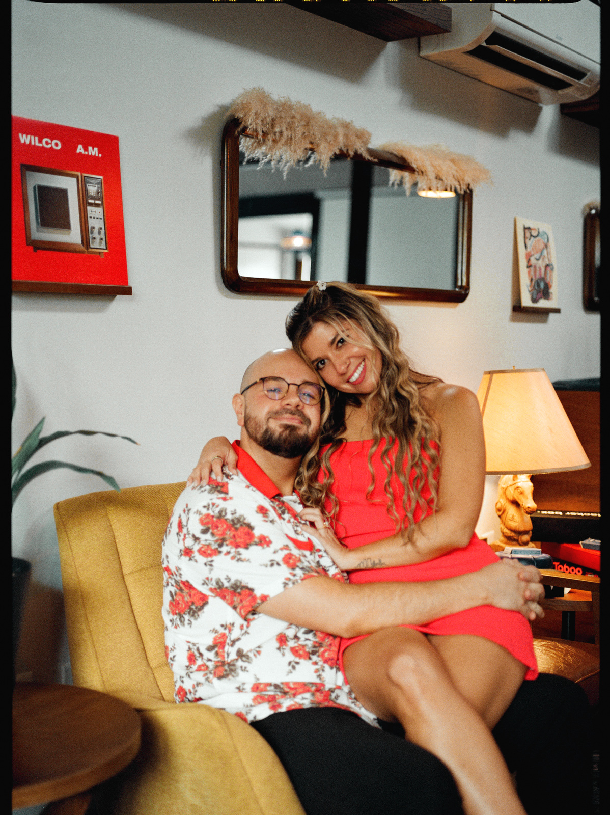Curled up together in a mustard armchair in a room of vintage furniture and lamplight.