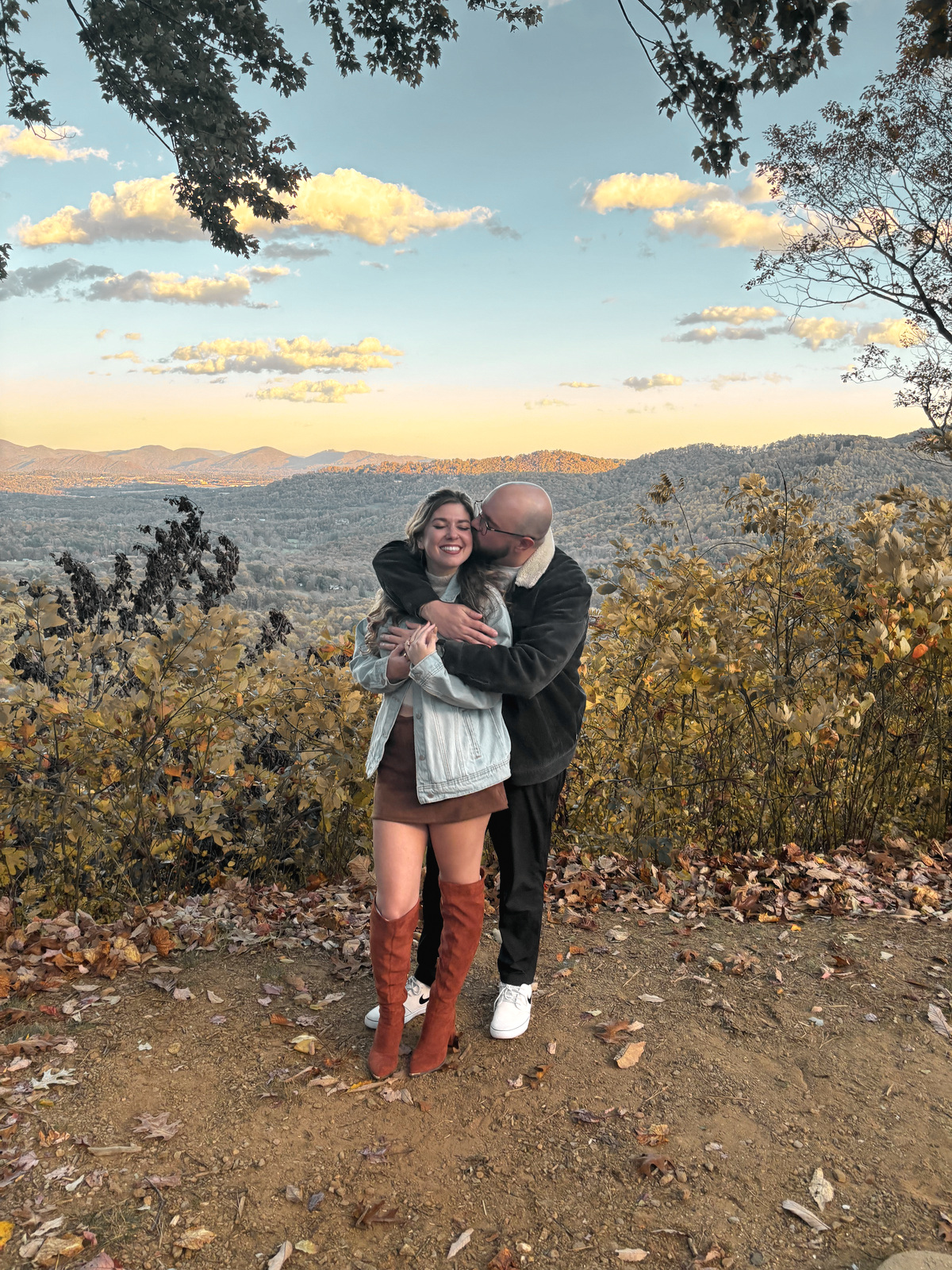 At the same overlook, one of them holding the other from behind, both laughing, autumn hills below.