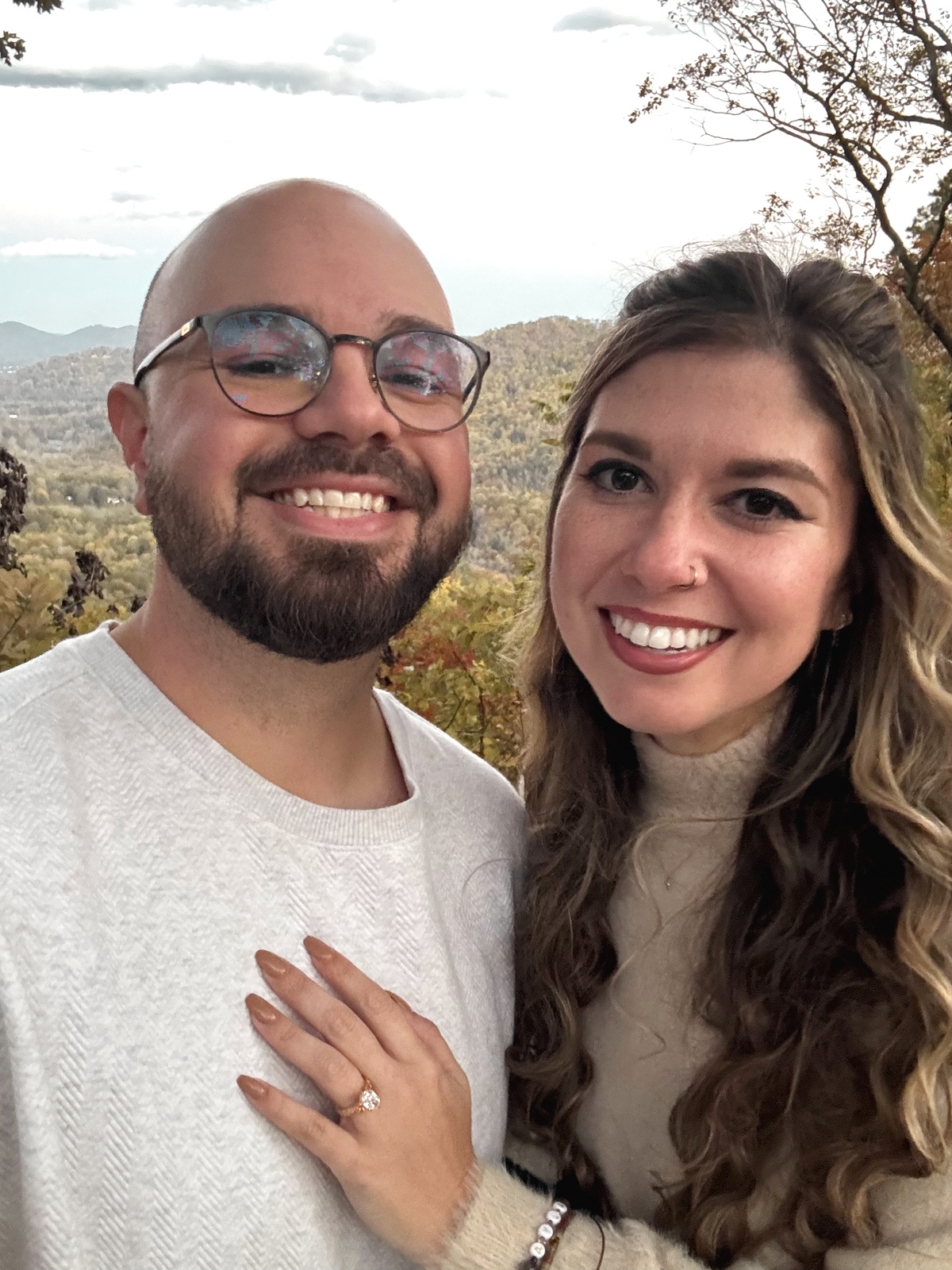 A close portrait of the two of them cheek to cheek, one hand resting on the other’s chest with an engagement ring on it.